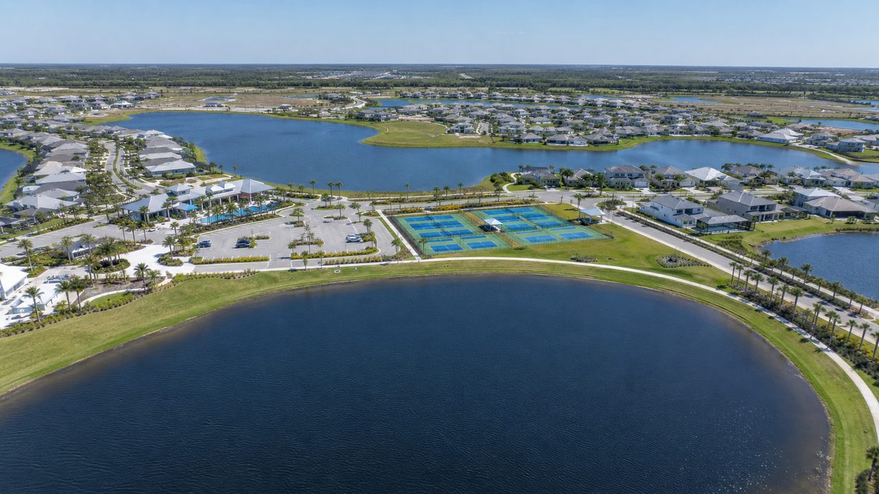Aerial view over SkySail in Naples showing the lake system, amenity campus, pickleball courts and surrounding homes