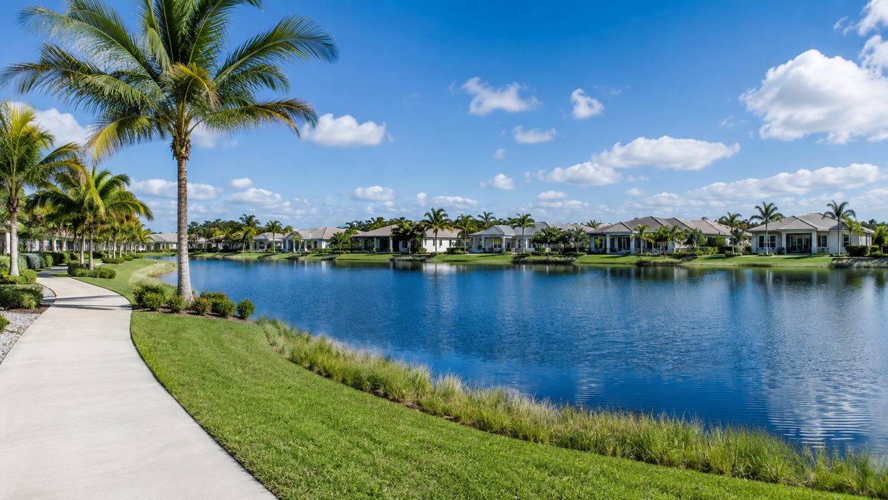 Lake at SkySail in Naples, Florida with a paved walking path, palm trees and lakefront homes across the water
